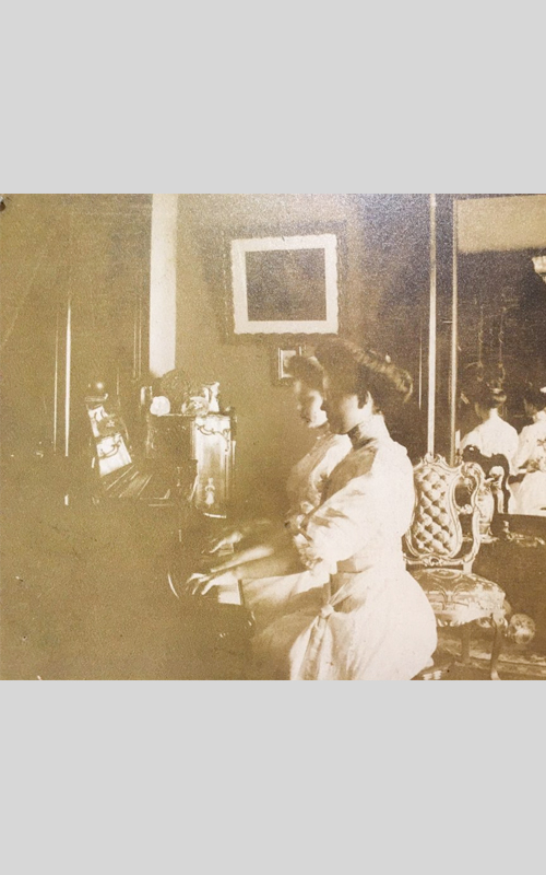 <h3>Piano Four Hands</h3>
<p><i>Photographer unknown</i></p>
<br>
<p><strong>Ca. 1900</strong></p>
<br>
<br>
<p>This unidentified photograph shows two women playing a single piano in a handsomely decorated house – presumably in Orient or East Marion. Like the hooked tapestry, it most likely depicts an evening musical entertainment in a private house.</p>