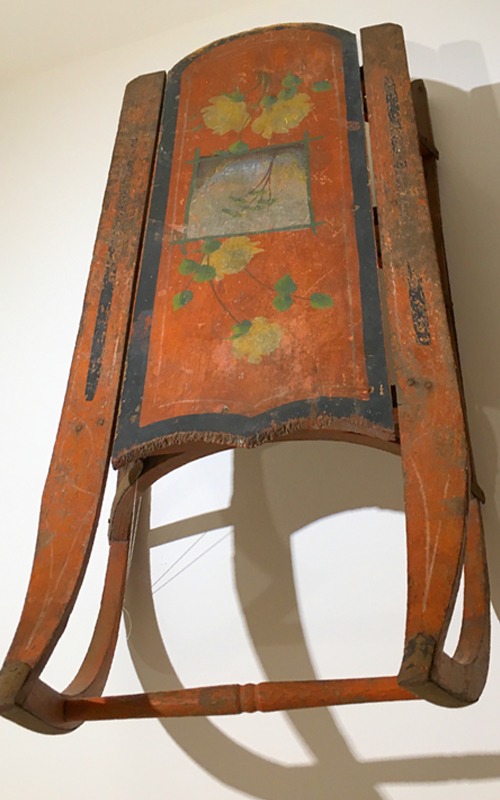 <h3>Sled</h3>
<br>
<p><i>Maker Unknown</i></p>
<br>
<strong>Late nineteenth / early twentieth century</strong>
<br>
<br>
<p>This colorful red sled has black stripes and yellow roses surrounding a tree that is painted in the center portion of the sled. Although the flexible flyer – a steerable sled – was invented as early as the 1880s, there were still many ordinary sleds like this one produced. They were often decorated, though were usually not as fanciful as the OHS sled. A sled like this one has become an iconic piece of Americana thanks to Orson Welles’ film <i>Citizen Kane.</i></p>