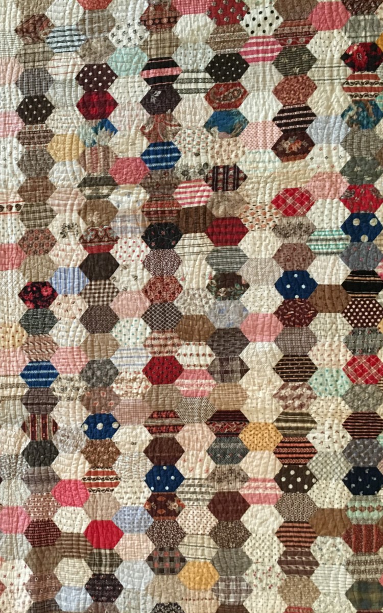 <h3>HEXAGONS</h3>
<br>
<p><strong>Pieced Quilt</strong></p>
<p><strong>Second half of the nineteenth century</strong></p>
<p><strong>Gift of Mrs. L.A. Van Kleeck</strong></p>
<br>
<p>This deceptively simple quilt design is made of a great many
connected, elongated hexagons. They are arranged vertically in
alternating rows of light and dark fabrics which gives some
structure to what otherwise seems a random design. Hexagons, a
form often used in quilt making, are usually of a more regular
shape and arranged to create a specific design. They are the basic
units of quilts known as Honeycomb, Grandmother’s Flower
Garden, and Mosaic. The piecing in this quilt involves a great
variety of nineteenth-century printed cotton fabrics. Women kept
scrap bags full of every bit of material that could be saved and
recycled. Fabrics are frequently useful for dating quilts – but
scrap bags could be used for years and even handed down from
generation to generation. Fabrics are therefore not always an
accurate guide to dating a quilt.</p>
<br>
<p>The quilting, or stitching, in this quilt is interesting because it is
in a pattern completely unrelated to the piecing of the hexagonalshaped
cottons. The quilting creates its own overall design in
what is known as a clamshell pattern.</p>