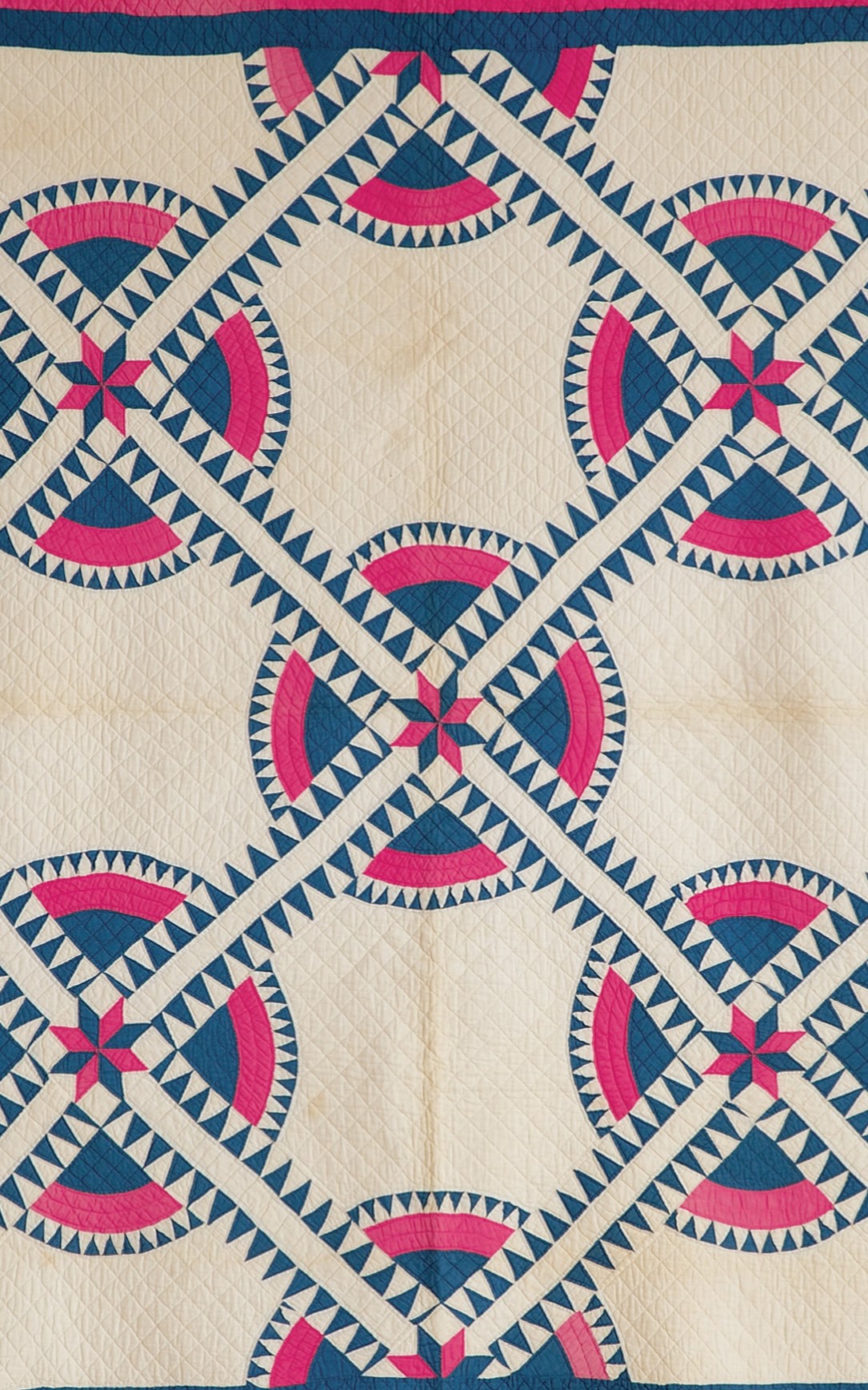 <h3>NEW YORK BEAUTY</h3>
<br>
<p><strong>Pieced Quilt</strong></p>
<p><strong>Second half of the nineteenth century</strong></p>
<p><strong>Gift of Mrs. Ernest Renard</strong></p>
<br>
<p>This striking pattern, known as New York Beauty, is fairly rare –
even in New York State where a quilt survey made in the 1980s
and 1990s turned up relatively few examples. The origin and
history of this pattern remain unknown. Its relative rarity probably
stems from the fact that it is considered a particularly difficult
pattern to make. An accomplished quilter is required to accurately
sew the hundreds of tiny triangles. This pattern is sometimes
called Crown of Thorns. The eight-pointed star at the center of
each divided circle where the overlaying bands cross is called a
Lemoyne Star and is based on a single diamond creating each
point of the star. The dominant stitching in the quilt is known as
crosshatch or grid quilting. This brightly colored New York
Beauty quilt is in remarkably good condition.</p>
<br>
</p>The donor was Helen Storey Renard. Her mother, Alice Storey,
was from Troy, New York, but the family summered in Orient. A
New York State provenance for this quilt is therefore likely but
not certain.</p>